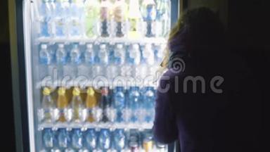 从穿紫色外套的年轻女人的背部看，从自动售货机上选择<strong>饮料</strong>。 库存录像。 <strong>饮料</strong>自动售货机